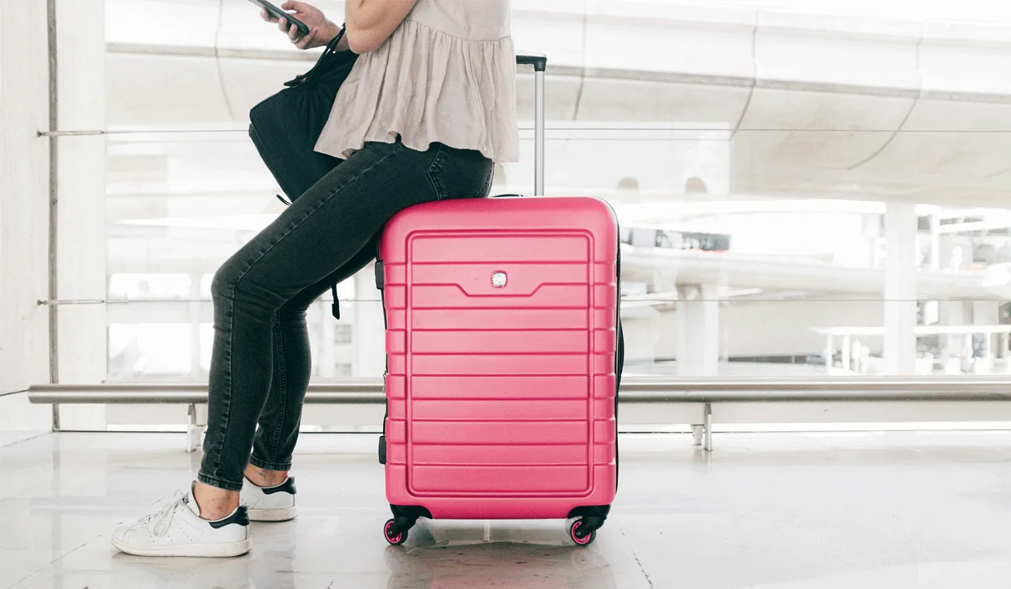 Mulher aguarda no terminal, sentada em cima de mala cor de rosa